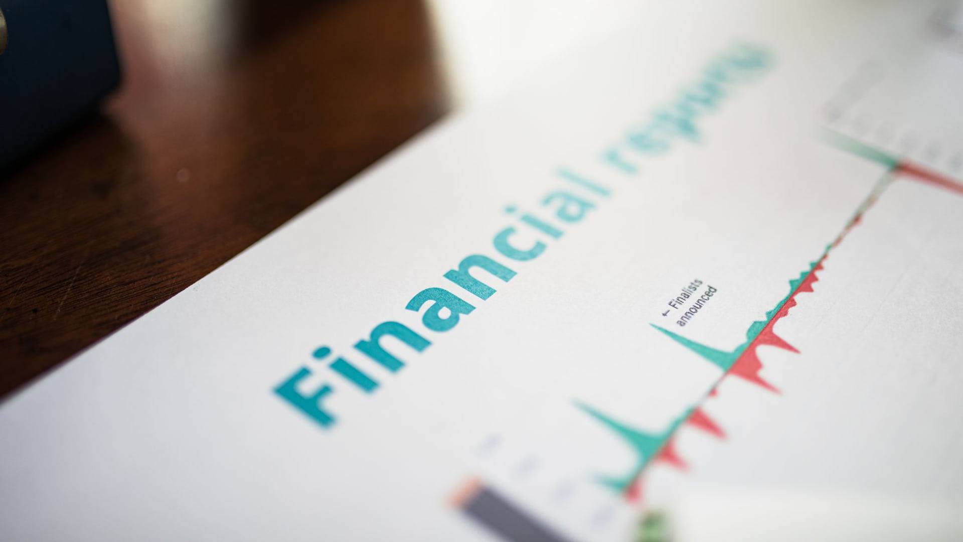Un dossier imprimé contenant des graphiques financiers posé sur un bureau à côté d'une facture d'électricité et d'une loupe.