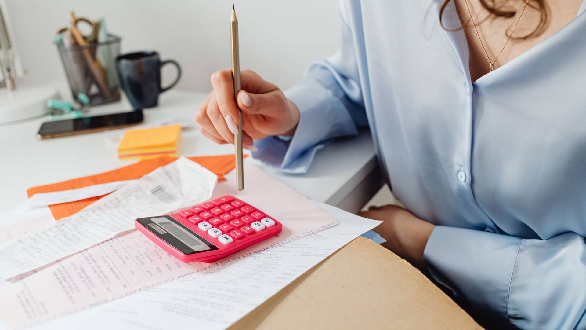 Une personne consulte un dossier de factures énergétiques avec une calculatrice et un tableau budgétaire sur un bureau.