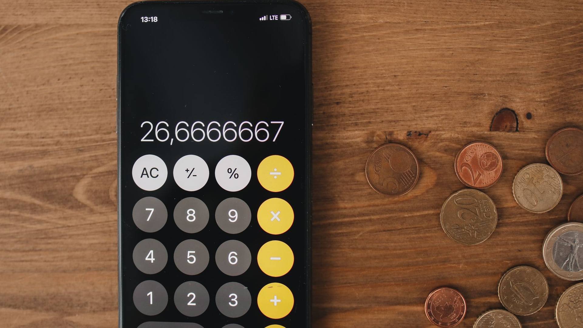 Un smartphone haut de gamme posé sur une table de bureau à côté d'une calculatrice et d'une feuille montrant un tableau de calculs.