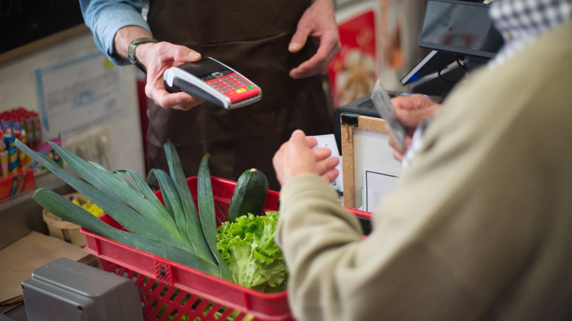 Personne analysant un ticket de caisse et une calculette à côté d'un panier de courses alimentaires