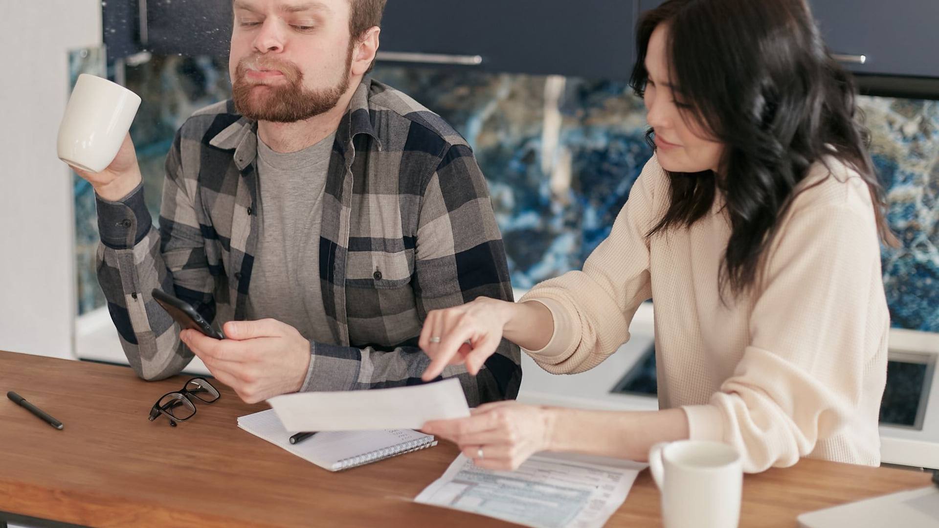 Une personne analysant une facture d'énergie sur une table avec une calculatrice à côté d'une tasse chaude en automne