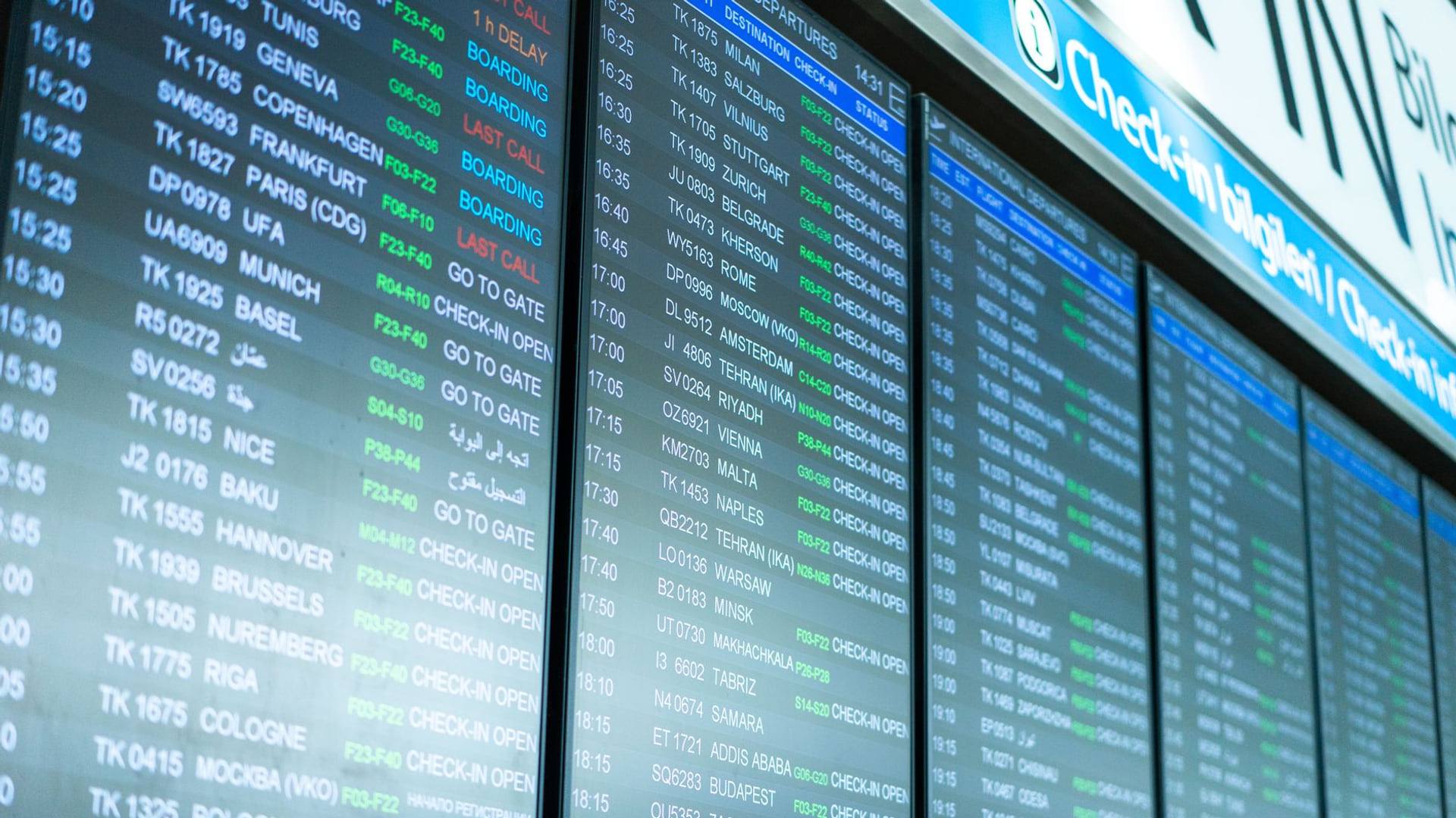 Panneau d'affichage d'un aéroport international indiquant des vols en retard devant des voyageurs attendant avec leurs bagages
