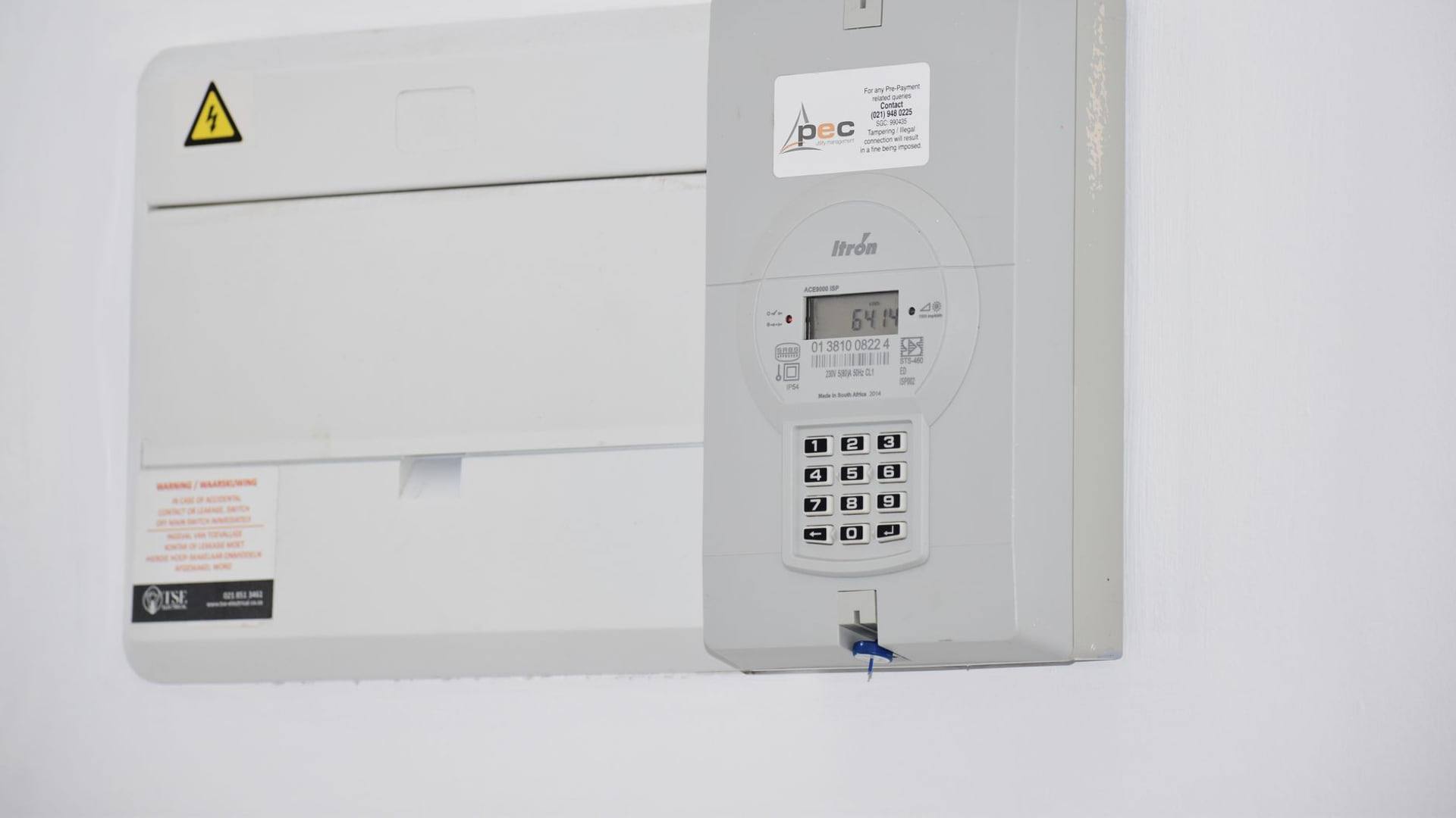 Un compteur d'électricité communicant accroché au mur à côté d'un tableau électrique domestique.