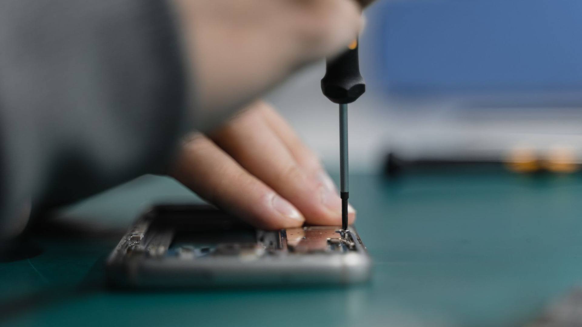 Un technicien dans un atelier examinant l'écran et le châssis d'un téléphone haut de gamme sous une lampe de précision.