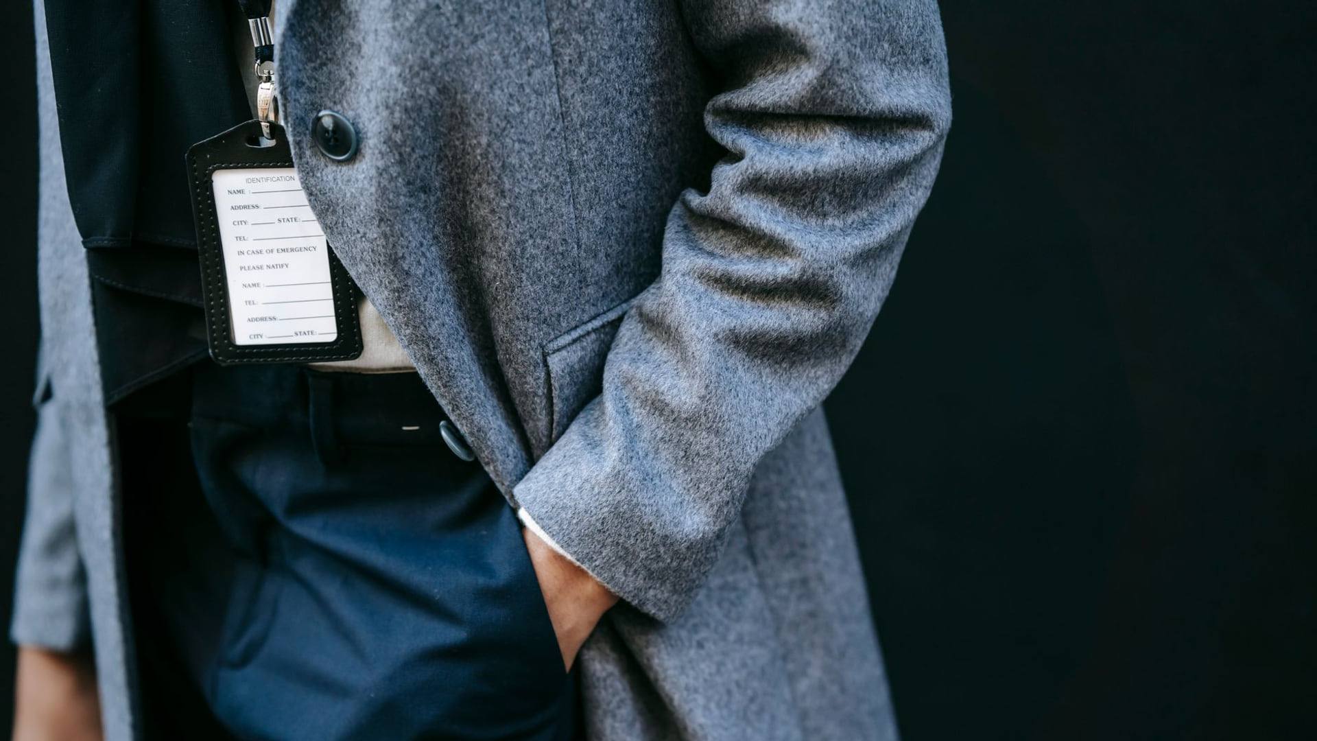 Une personne inspectant à la loupe les coutures et l'étiquette de composition d'un manteau en laine posé sur une table en bois.
