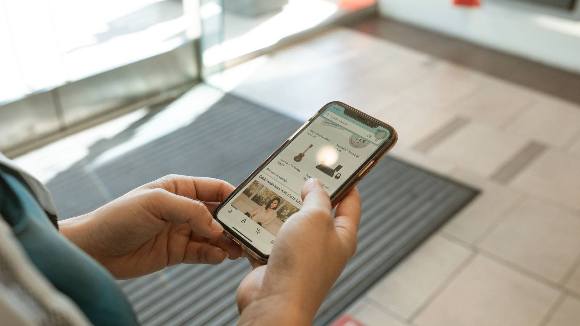 Une personne consulte un smartphone affichant un écran de panier d'achat avec plusieurs remises appliquées à côté d'une carte de fidélité.