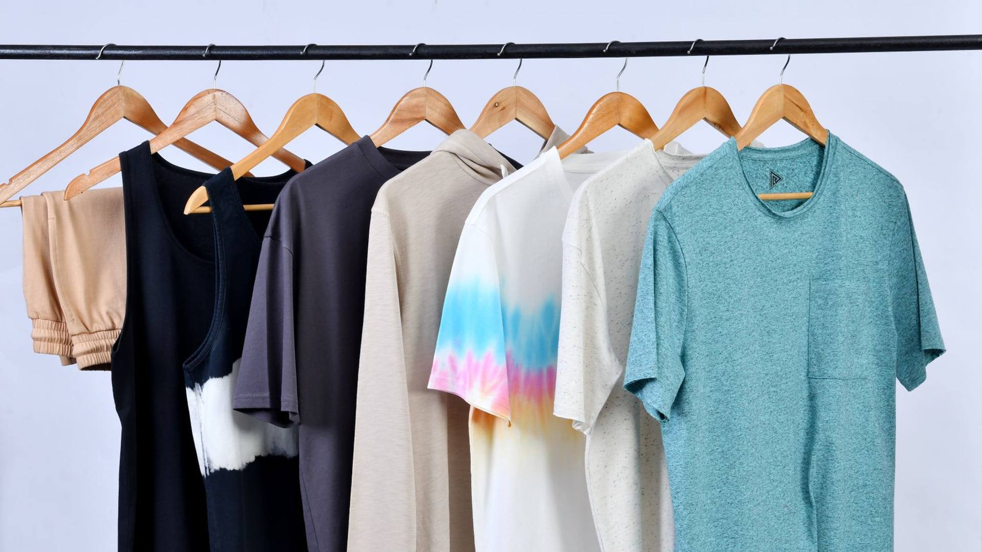 Une personne organisant un dressing comportant un mélange de vêtements basiques et de pièces structurées sur des cintres en bois