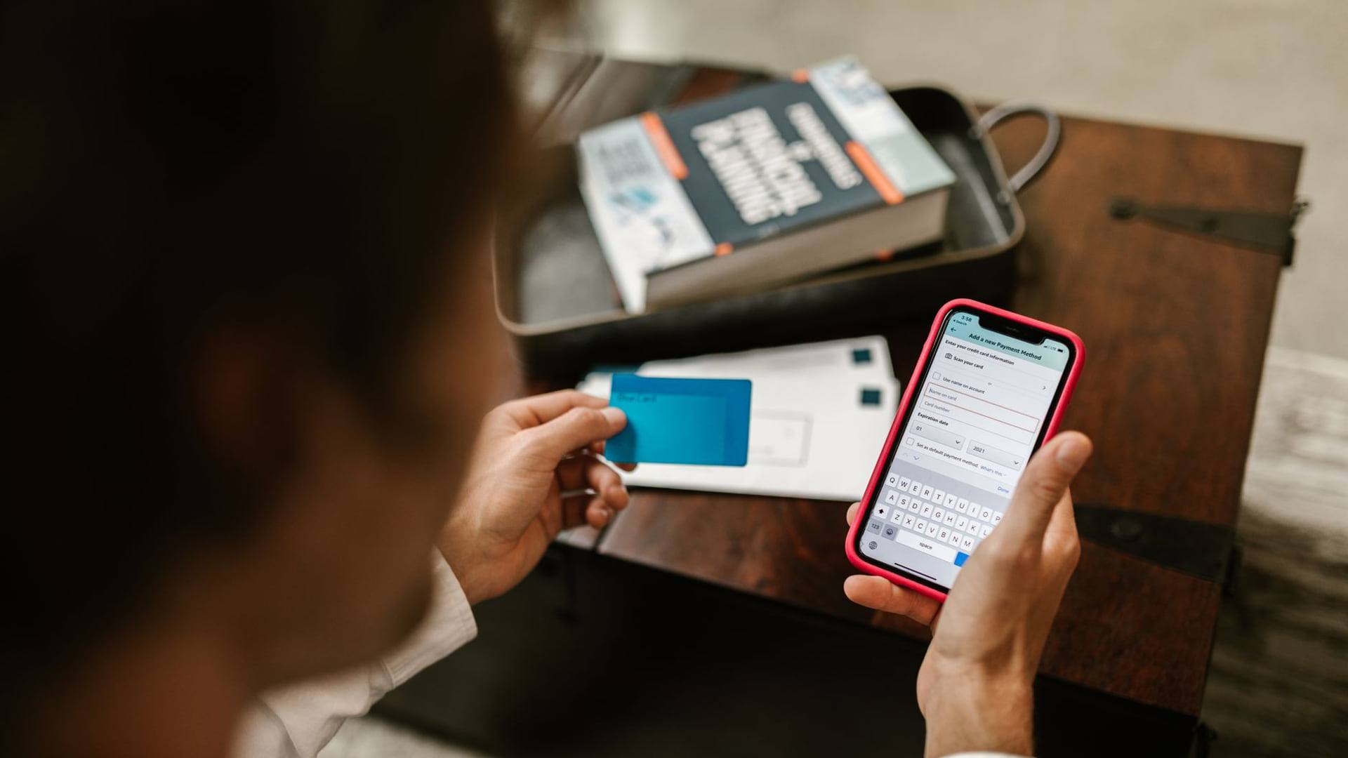 Une personne consultant son écran de téléphone avec une carte bancaire posée à côté d'un sac de shopping