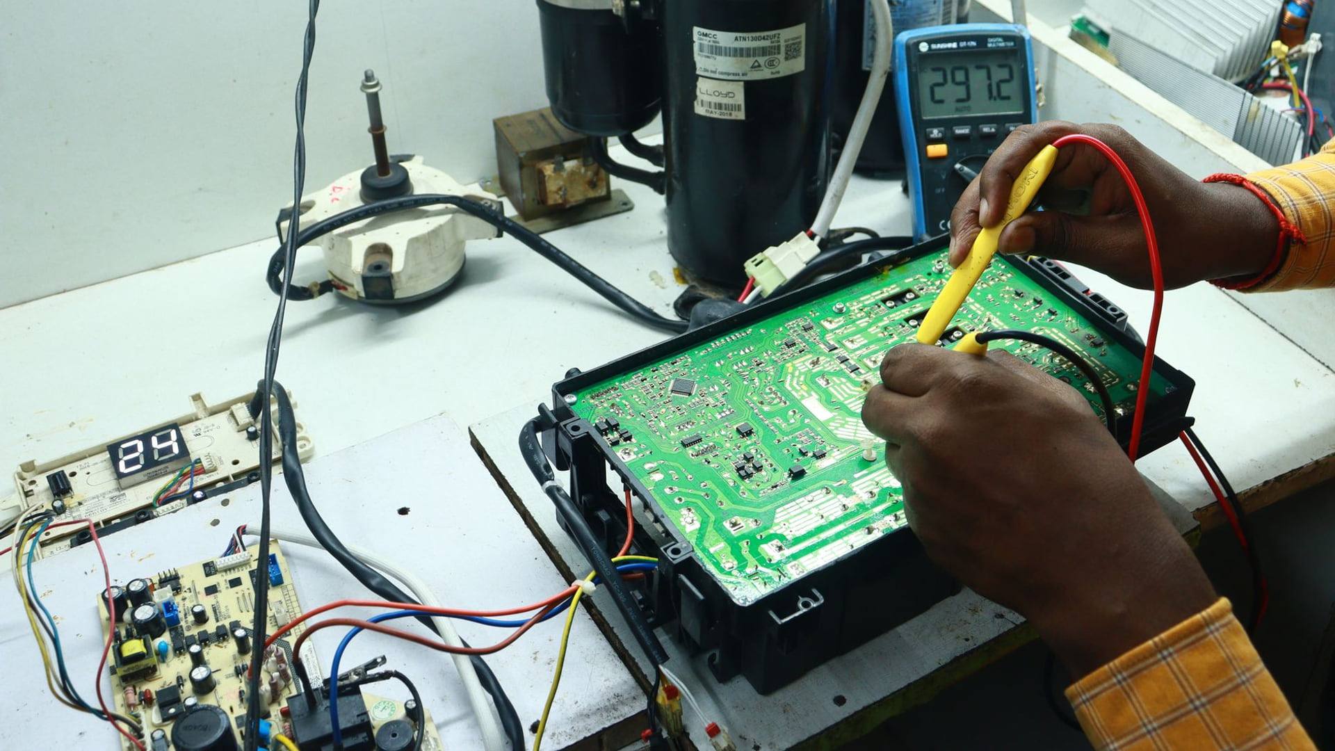 Un réparateur d'électroménager analyse les composants électroniques d'une machine à laver avec un appareil de mesure.