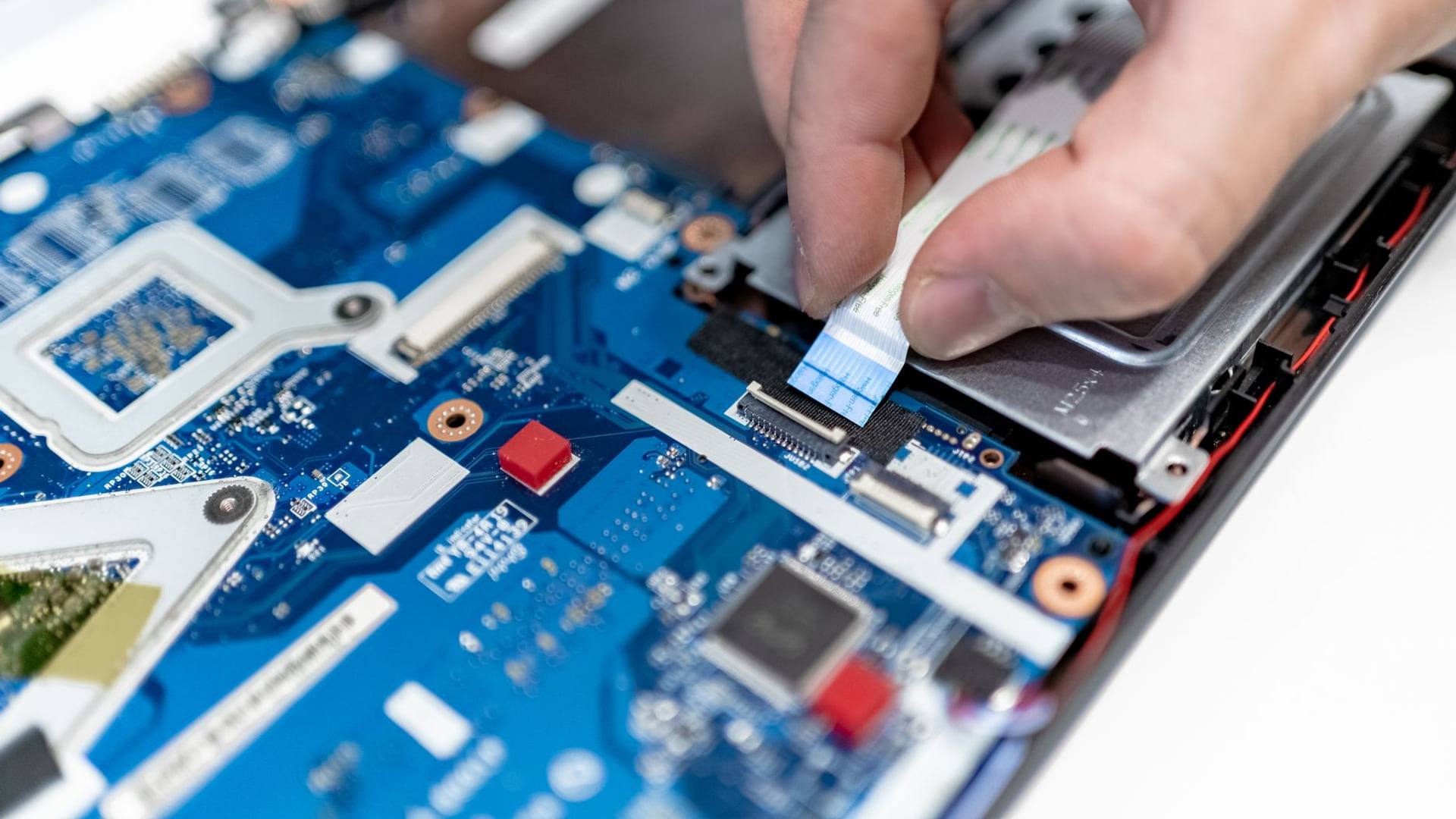 Un technicien inspecte le composant interne d'un appareil électronique sous la lampe d'un atelier de réparation.