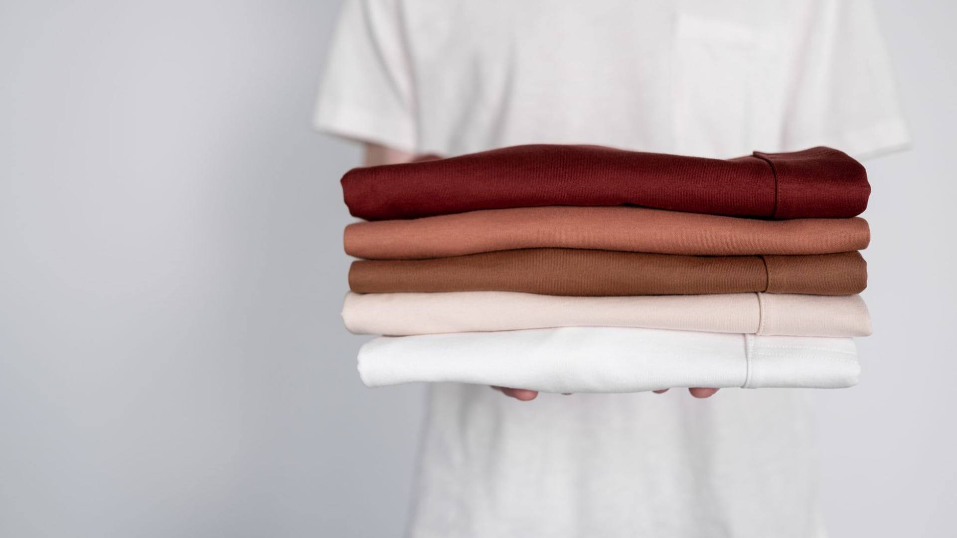 Une personne soigneusement pliée organise des vêtements d'occasion sur une table en bois clair pour prendre des photographies.