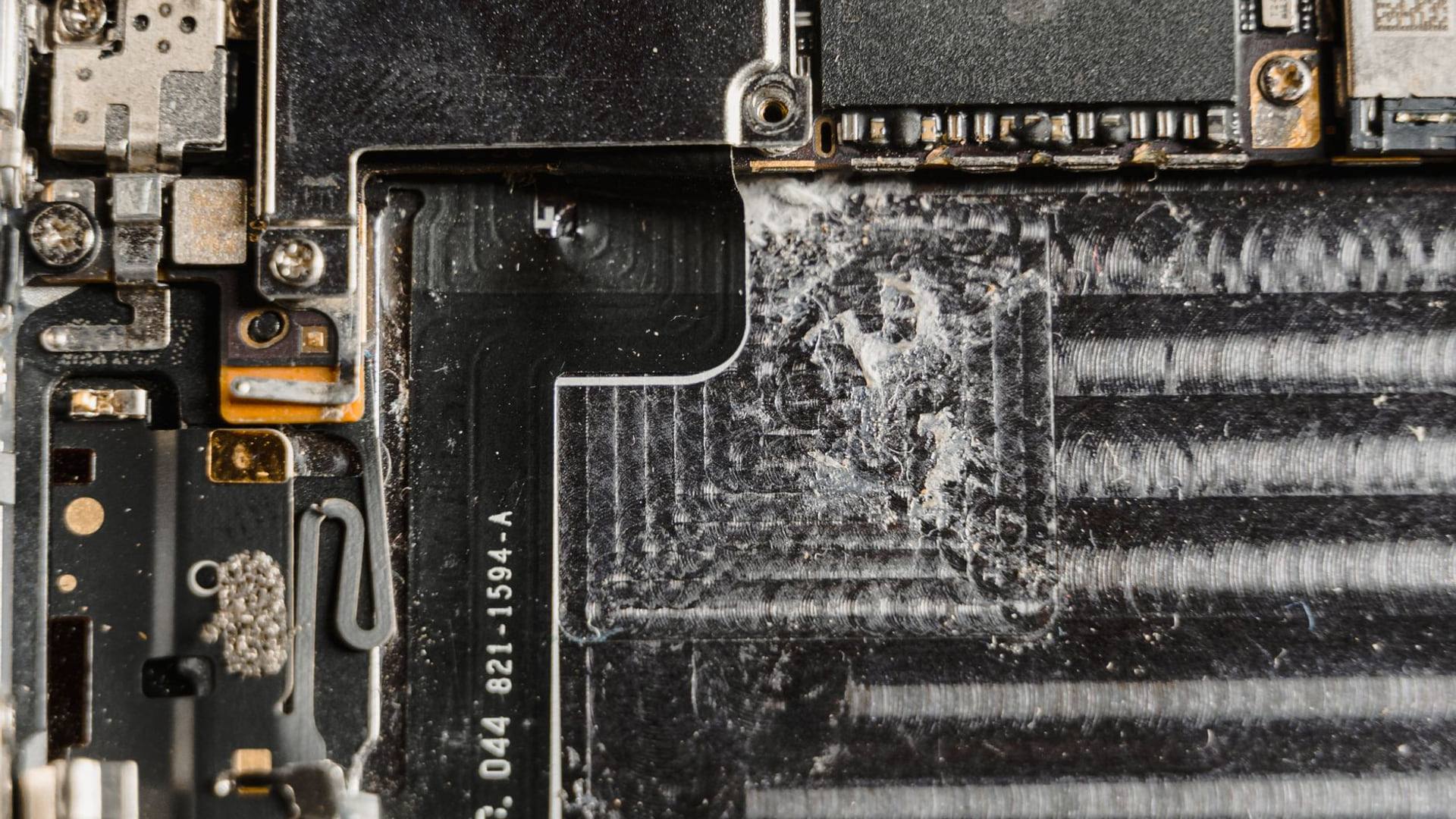 Un technicien spécialisé inspecte les composants internes d'un smartphone noir posé sur un tapis de travail antistatique.