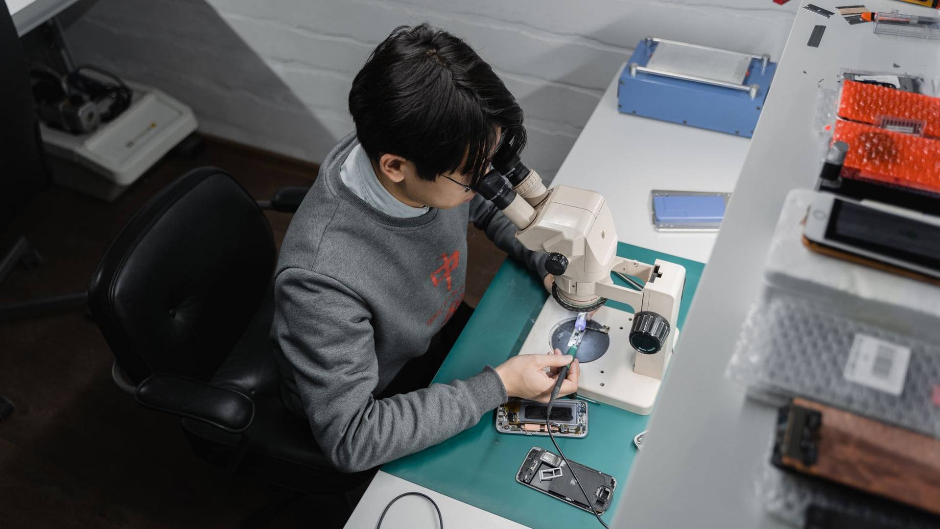 Un technicien mesurant l'état de la batterie d'un smartphone reconditionné à l'aide d'un appareil de diagnostic sur un plan de travail.